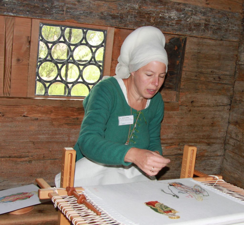 Dr Jessica Grimm demonstrating Medieval Goldwork Embroidery in period clothing.