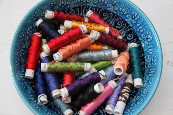 Ceramic bowl containing many spools of coloured embroidery silks.