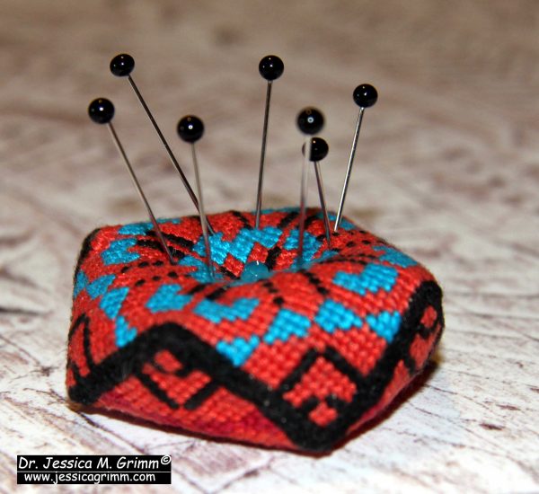 Embroidered pincushion with pins.