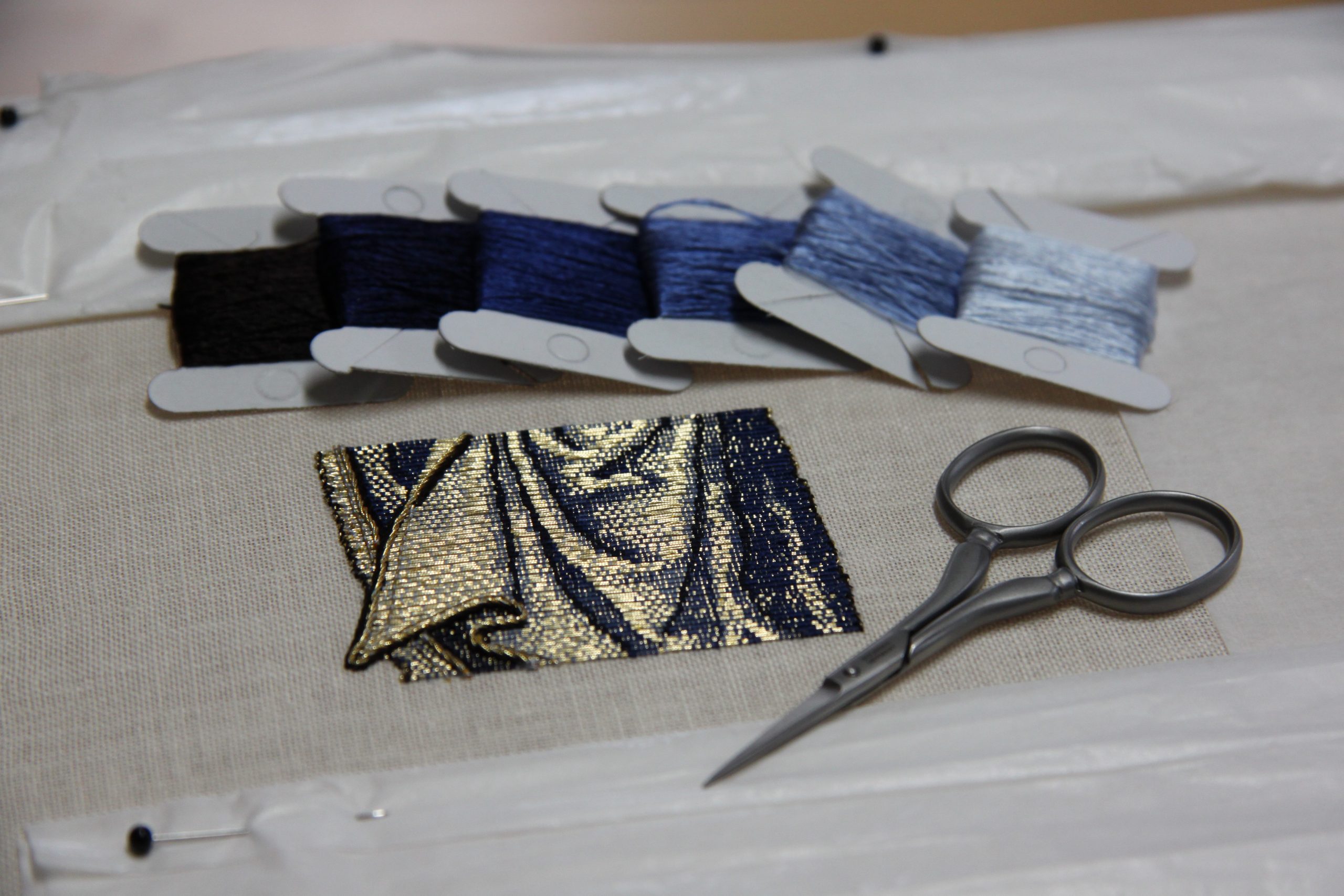 Learn medieval goldwork embroidery. Goldwork embroidery sample with bobbins with silk and scissors.