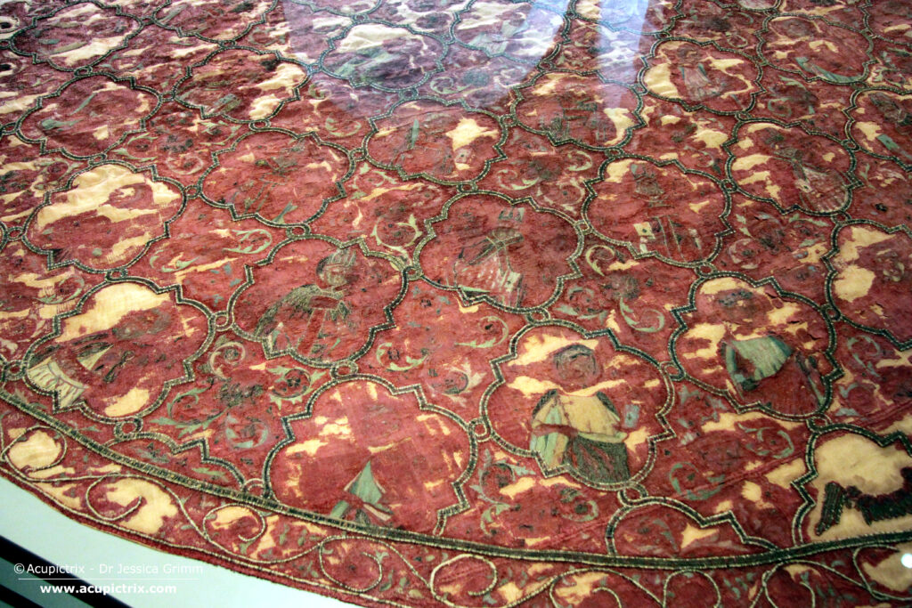 Italian embroidery - A large red cope laying flat in a museum display case.