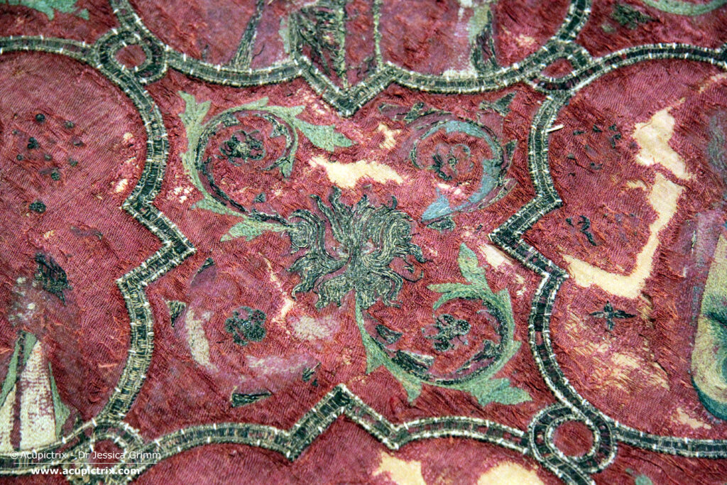 Italian embroidery - A large red cope laying flat in a museum display case.
