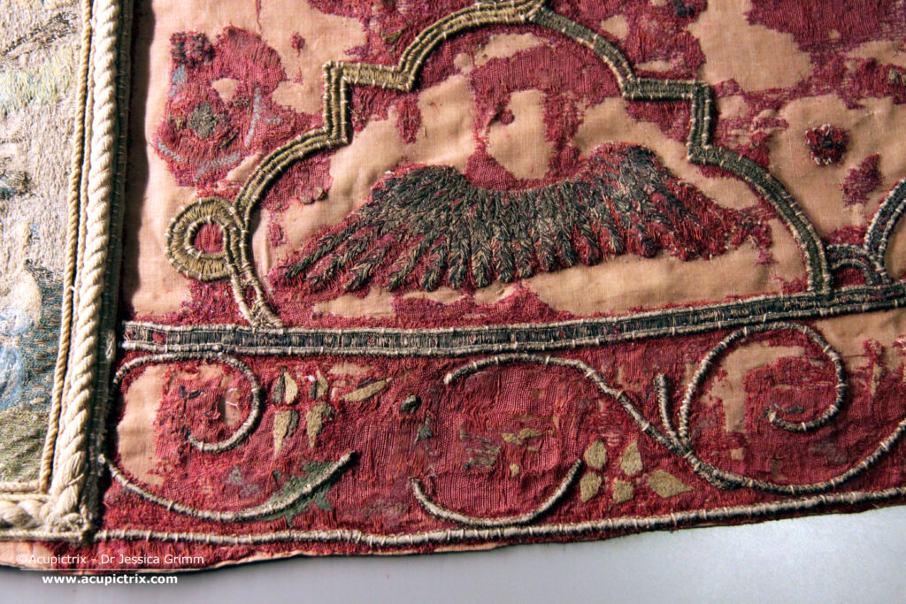 Italian embroidery - A large red cope laying flat in a museum display case.