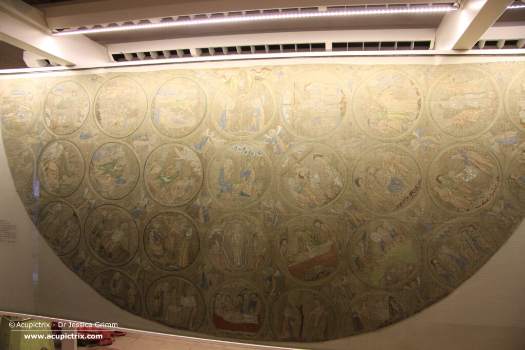 Opus anglicanum - a multi coloured embroidered semi circular vestment in a display case